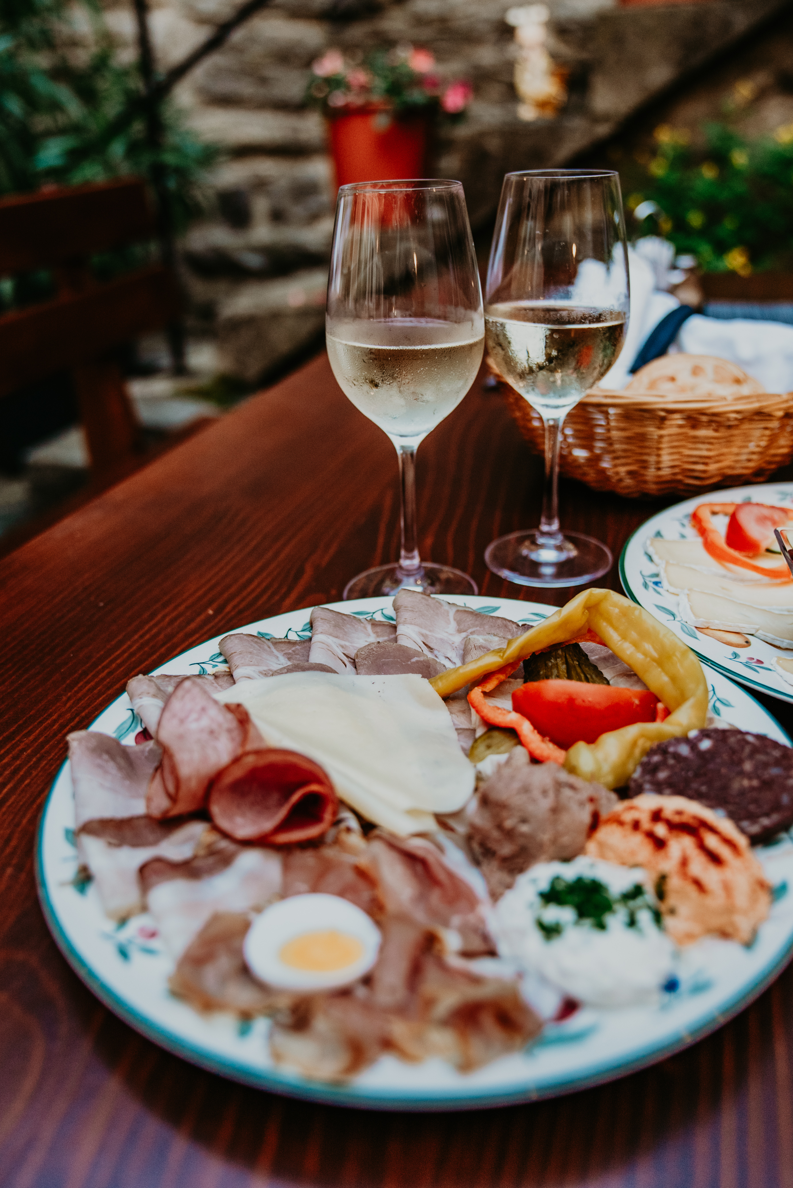 Ein Bild zeigt eine Brettljause beim Heurigen und zwei Gläser Weißwein.