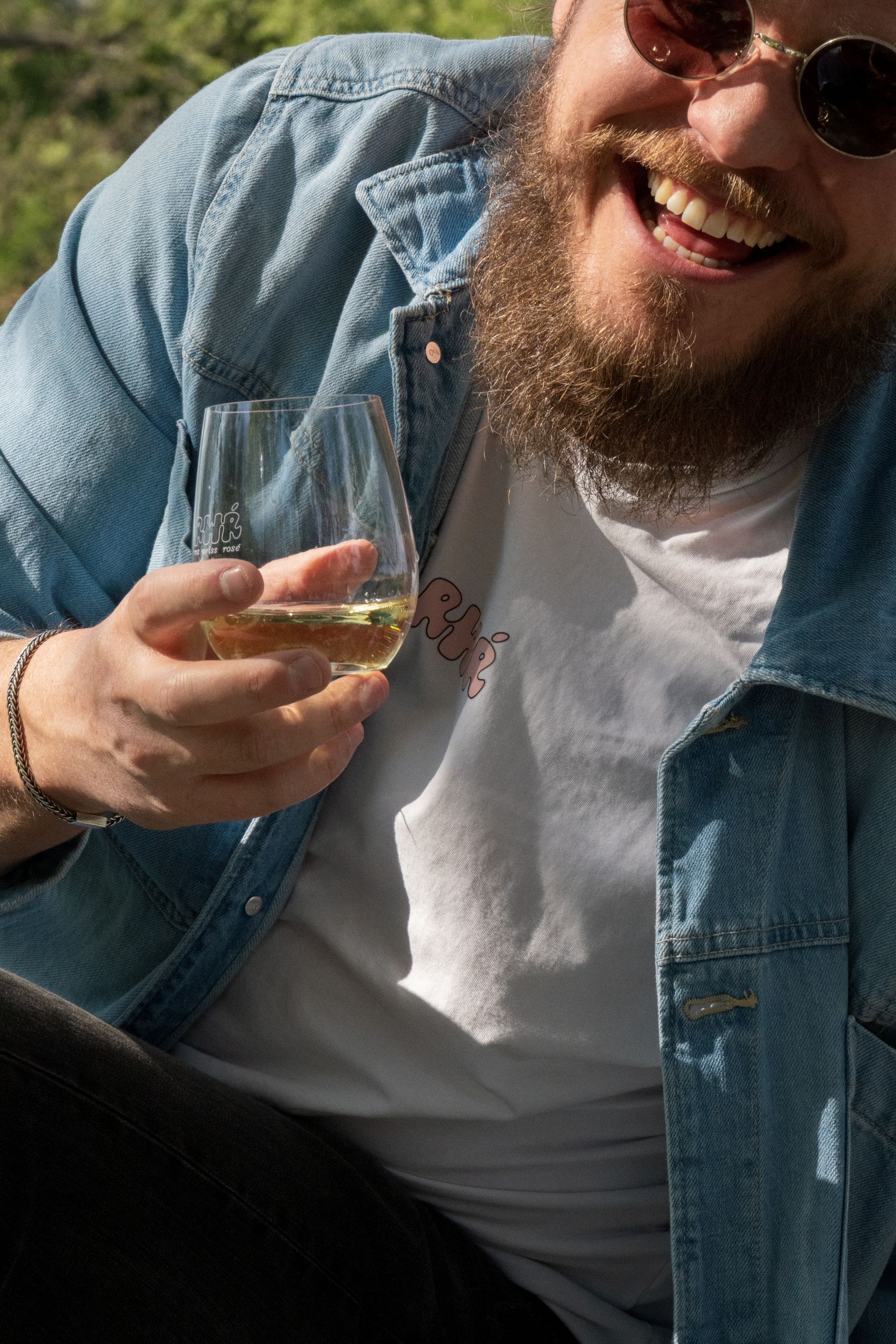 Ein junger Mann trinkt Weißwein aus Österreich und lacht.