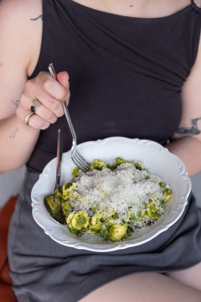 Eine junge Frau isst Pasta mit Löwenzahnpesto