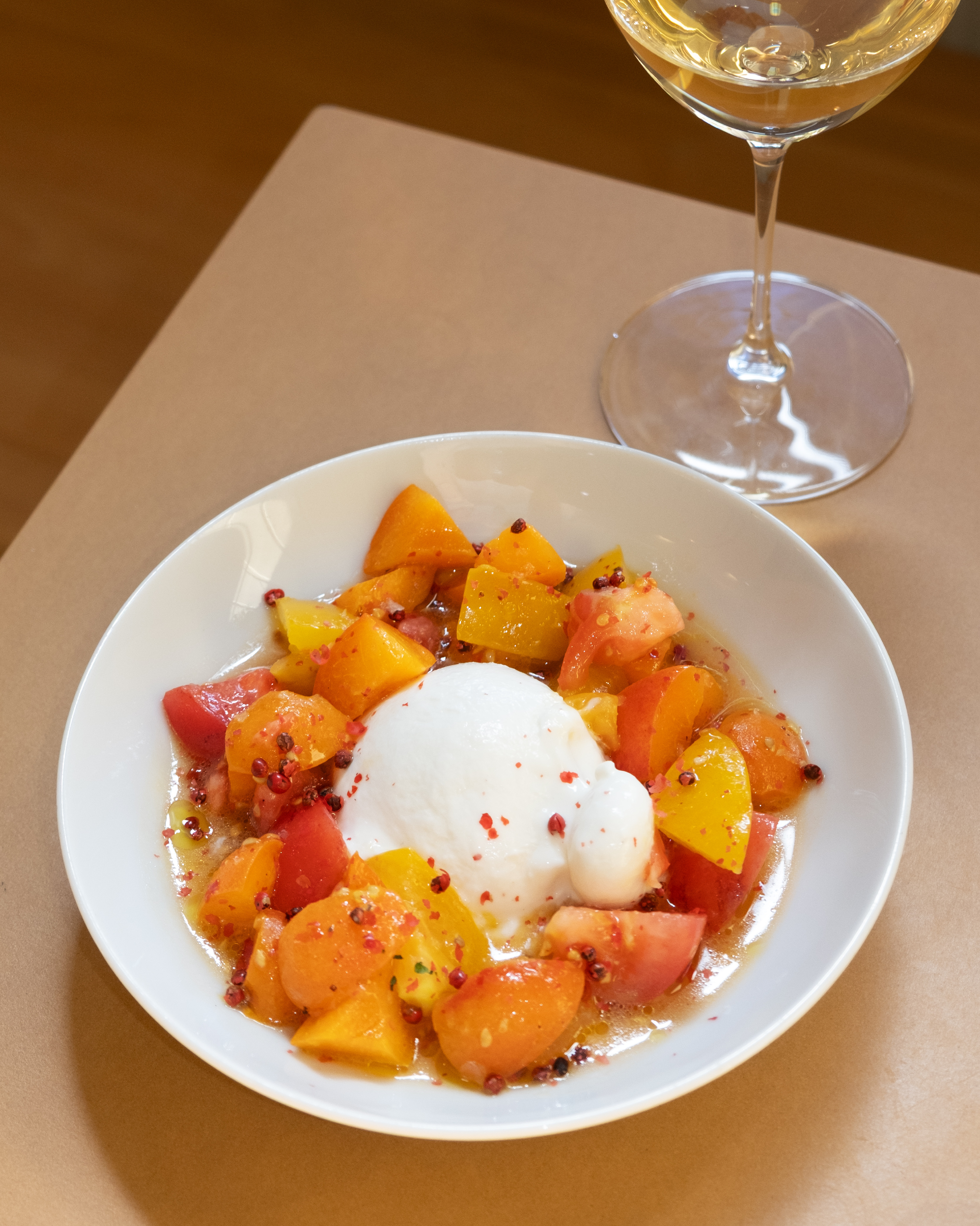 Das Bild zeigt das Gericht Burrata mit Marillen und Tomaten und ein Glas Gelber Muskateller.