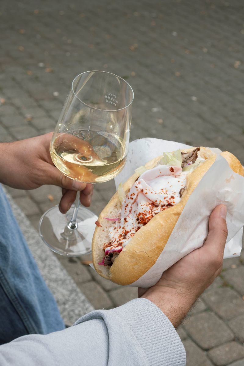 Ein junger Mann hält einen Döner und ein Glas Weißwein.